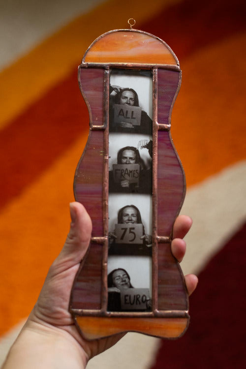 Colorful stained glass frame with photobooth photos inside, held by a hand against an orange background