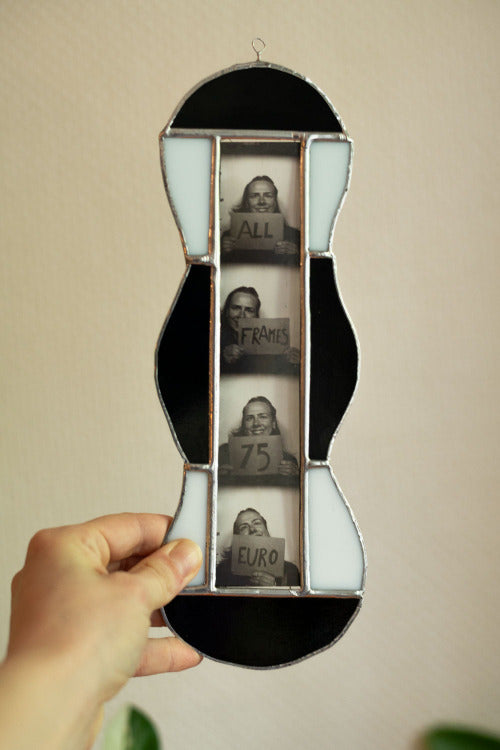 Black and white stained glass frame with photobooth photos inside, held by a hand against a beige background
