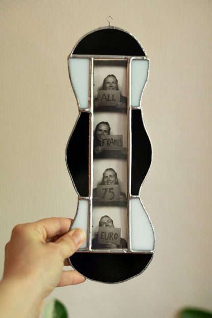 Black and white stained glass frame with photobooth photos inside, held by a hand against a beige background