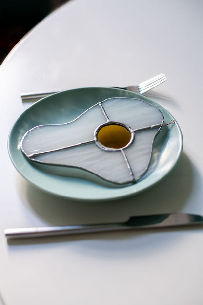 Teal plate with a decorative egg-shaped stained glass artwork, fork, knife, and glass on a white surface.