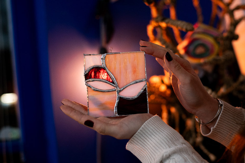 Two hands holding a stained glass art work against a colourful, cosy background