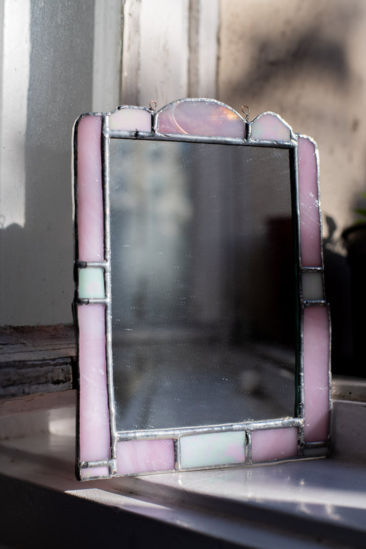 Stained glass mirror with a pink and white frame on a surface.
