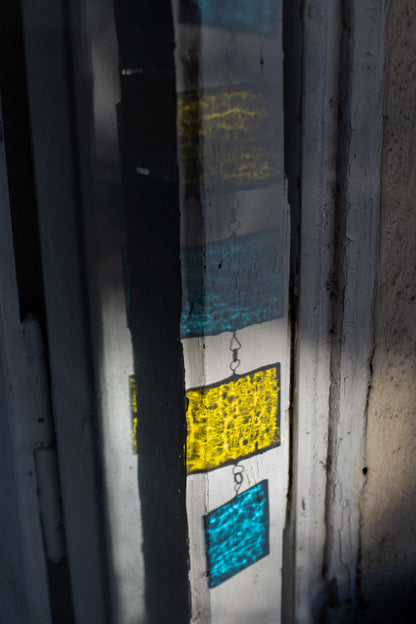 Yellow and blue shadow of a stained glass suncatcher against a white window frame