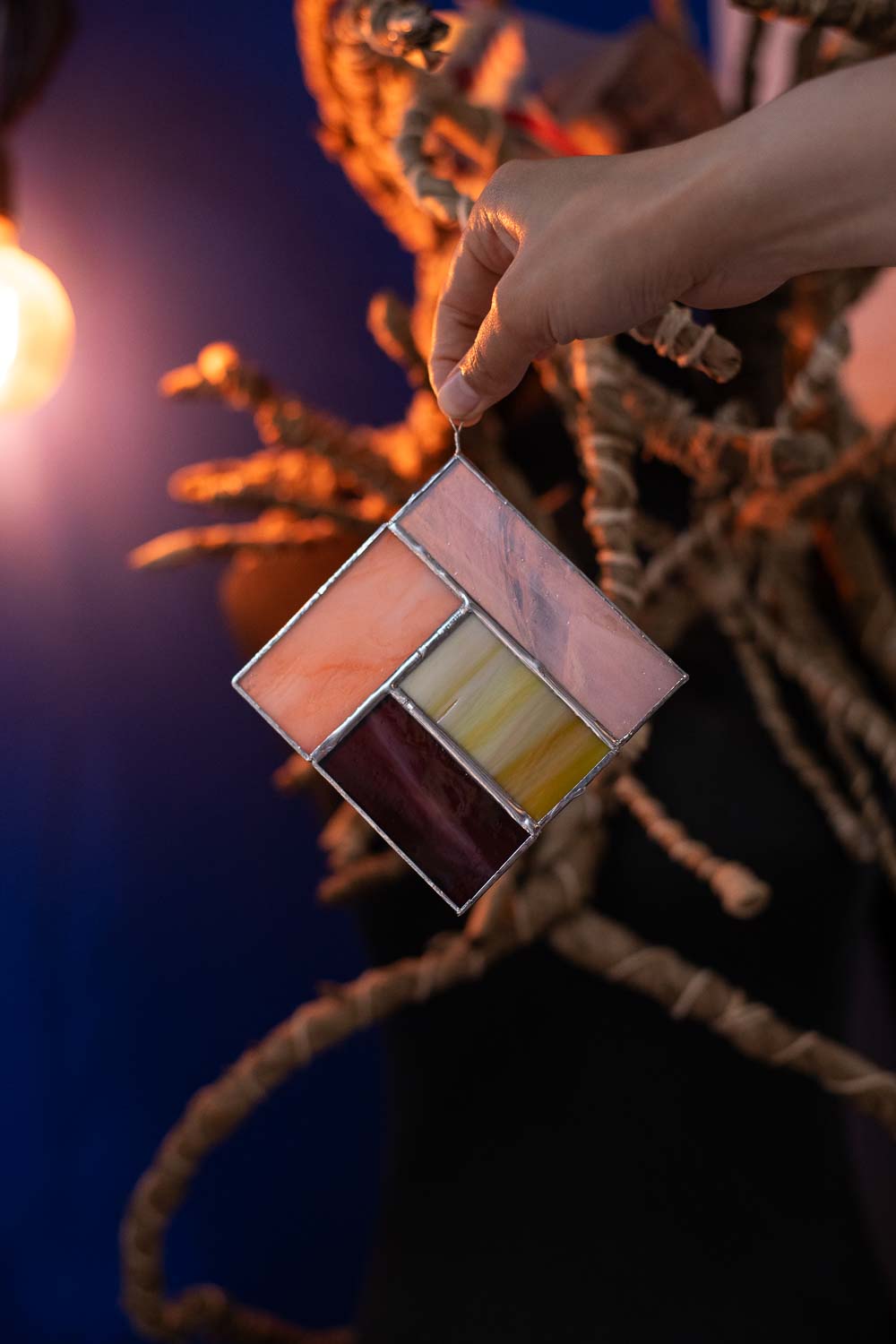 Hand holding a stained glass panel with warm colors against a blurred background