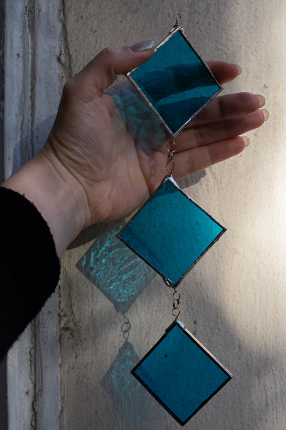 Hand holding a set of blue diamond-shaped stained glass pieces against a neutral background