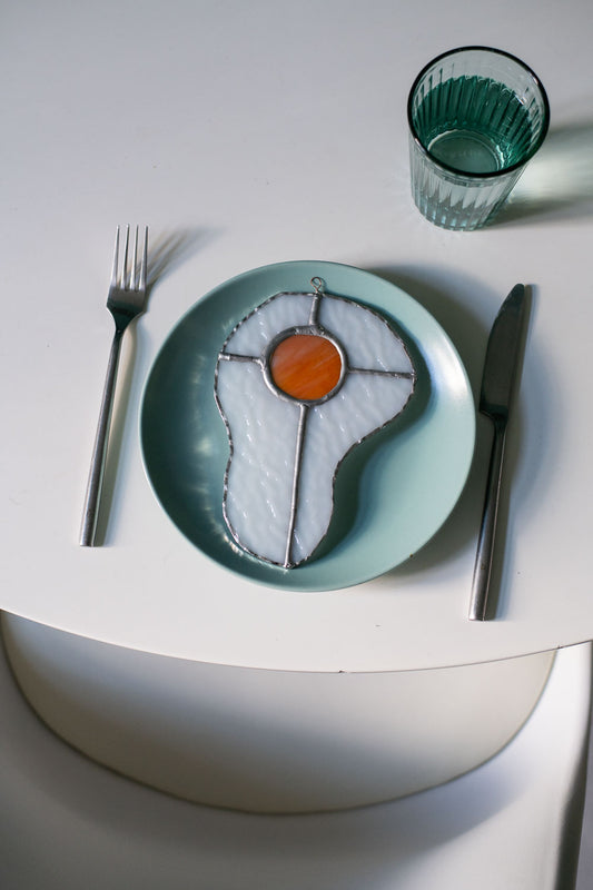 Teal plate with a decorative egg-shaped stained glass artwork, fork, knife, and glass on a white surface.