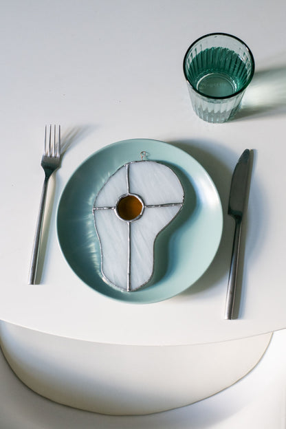 Teal plate with a decorative egg-shaped stained glass artwork, fork, knife, and glass on a white surface.