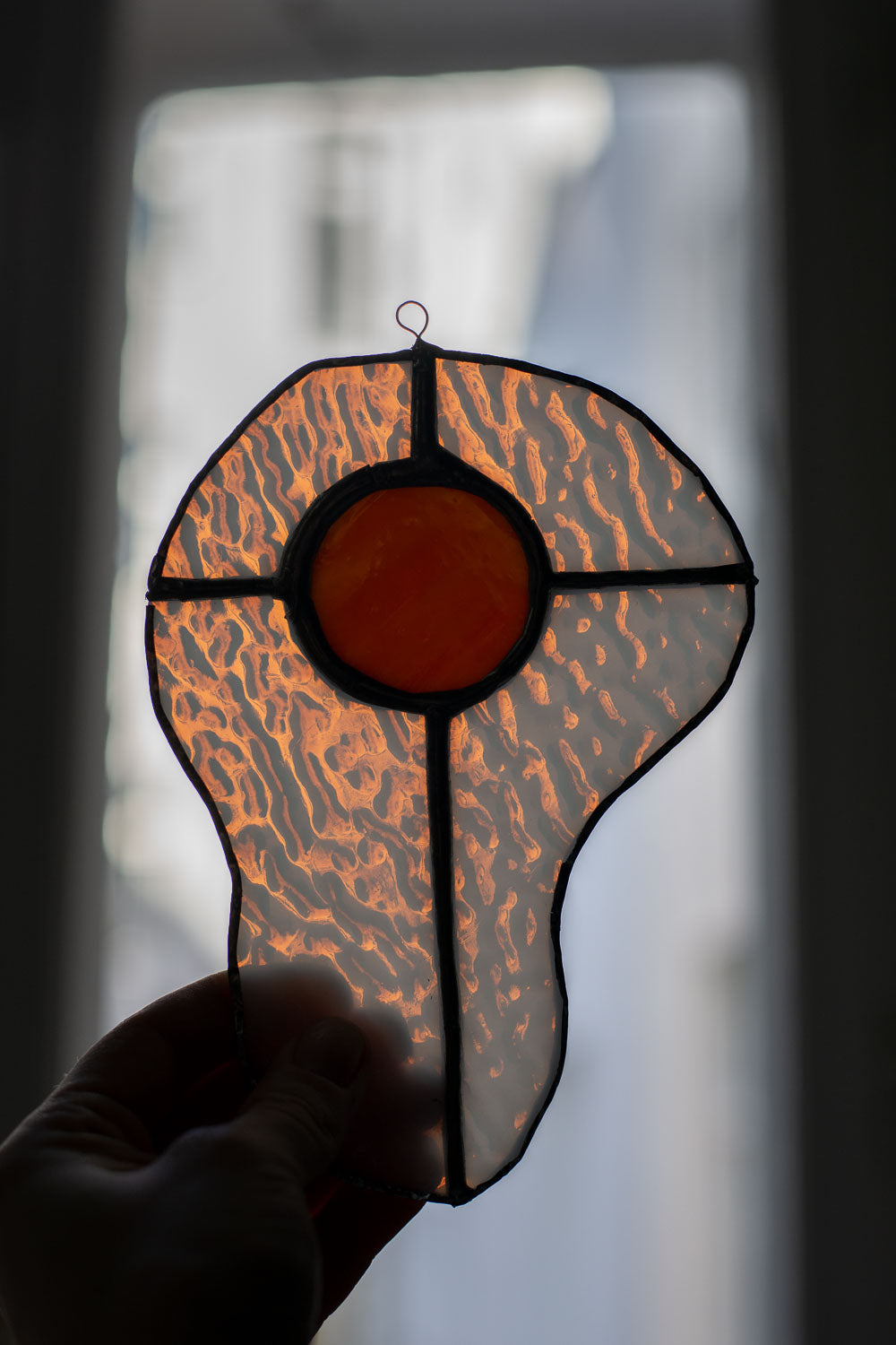 Stained glass window panel in an egg-shaped design held by a hand against a blurred background