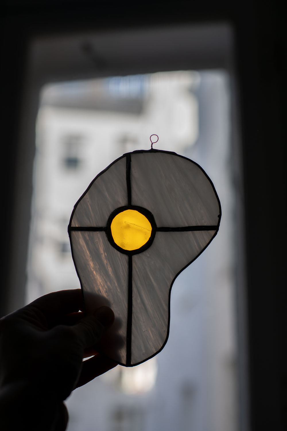 Egg-shaped stained glass window panel held against a blurred cityscape background