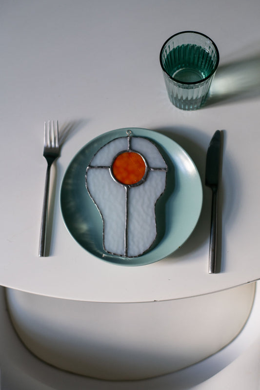 Teal plate with a decorative egg-shaped stained glass artwork, fork, knife, and glass on a white surface.