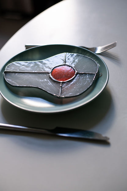 Teal plate with a decorative egg-shaped stained glass artwork, fork, knife, and glass on a white surface.