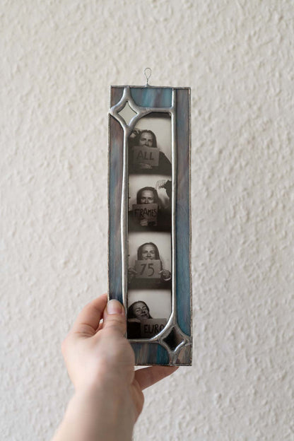Hand holding a vintage-style photo frame with black and white photos inside against a plain wall.