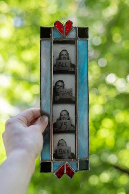 Stained glass picture frame held against a blurred green outdoor background.