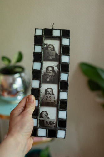 Film strip in a black and white frame held by a hand against a blurred indoor background