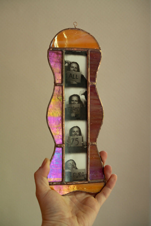 Colorful stained glass frame with photobooth photos inside, held by a hand against a beige background