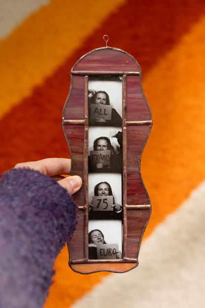 Colorful stained glass frame with photobooth photos inside, held by a hand against an orange background