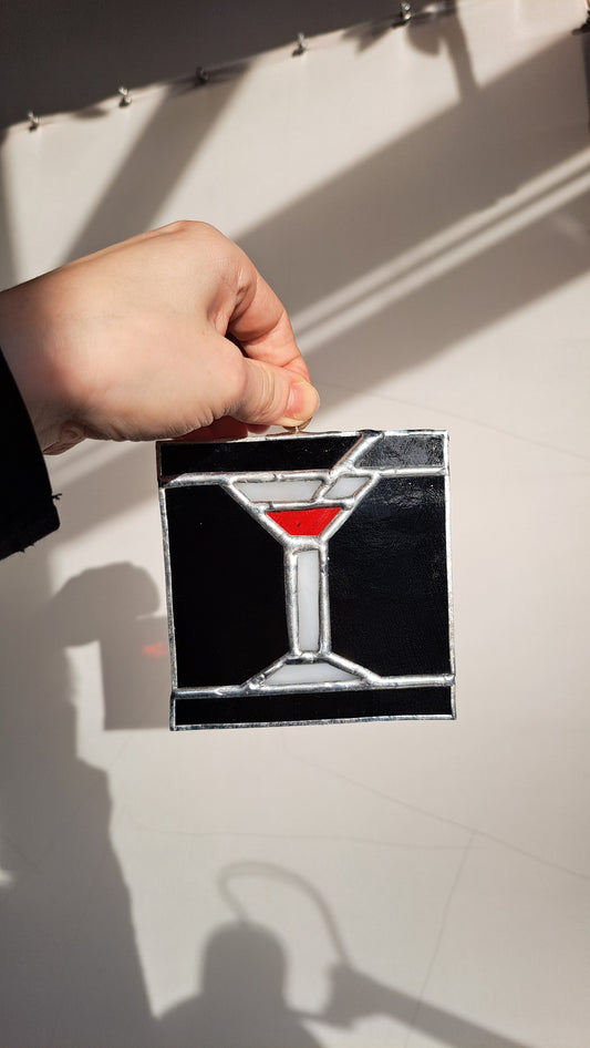 Hand holding a stained glass artwork with a black and red design of a martini cocktail