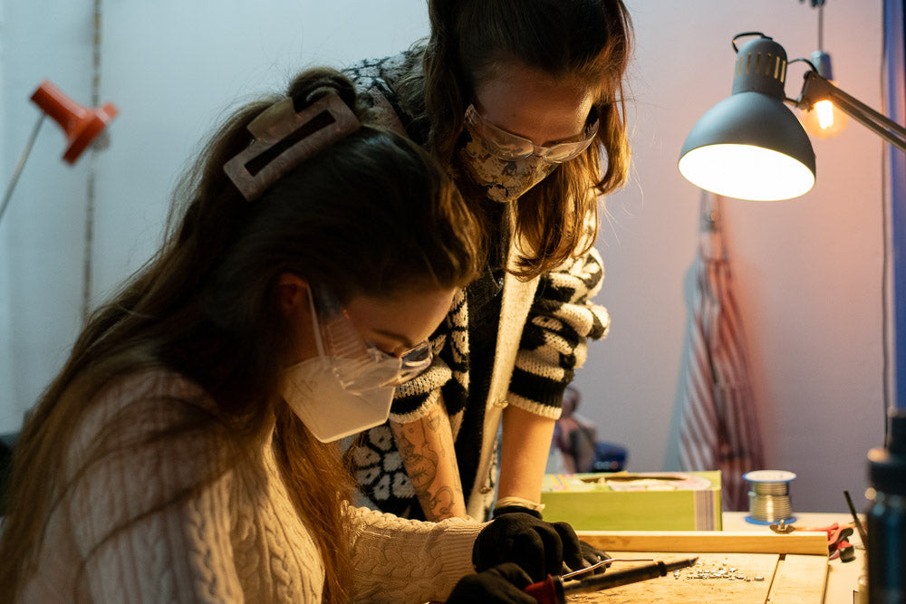 Two people working on a project with tools and a lamp in a workshop setting.