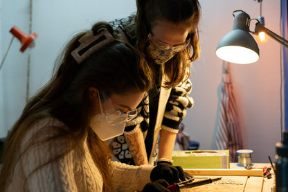 Two people working on a project with tools and a lamp in a workshop setting.